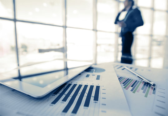 Business man in the background with financial charts in the foreground on a table